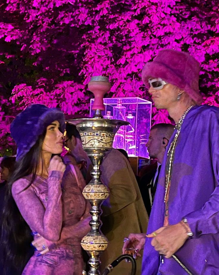 two people dressed in costume standing next to a large metal lamp with purple lights on it