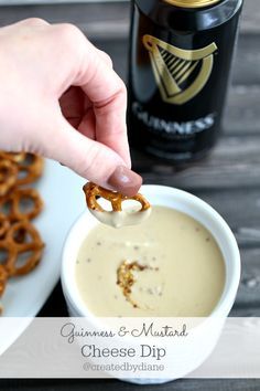 a person dipping pretzels into a bowl of cheese dip with a beer in the background