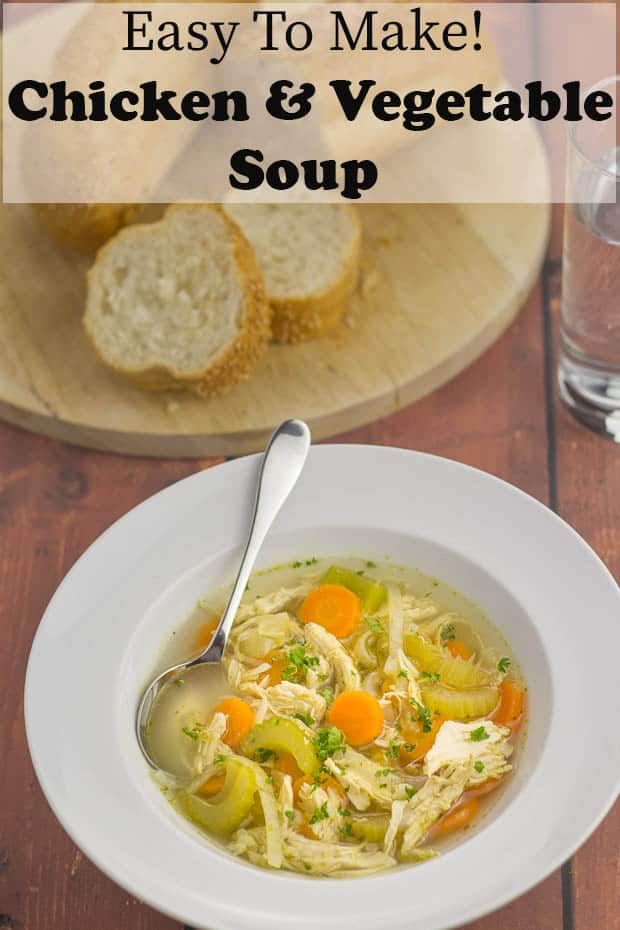 chicken and vegetable soup in a white bowl on a wooden table with slices of bread