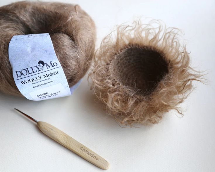 the woolly mohair is next to a ball of yarn and a knitting needle