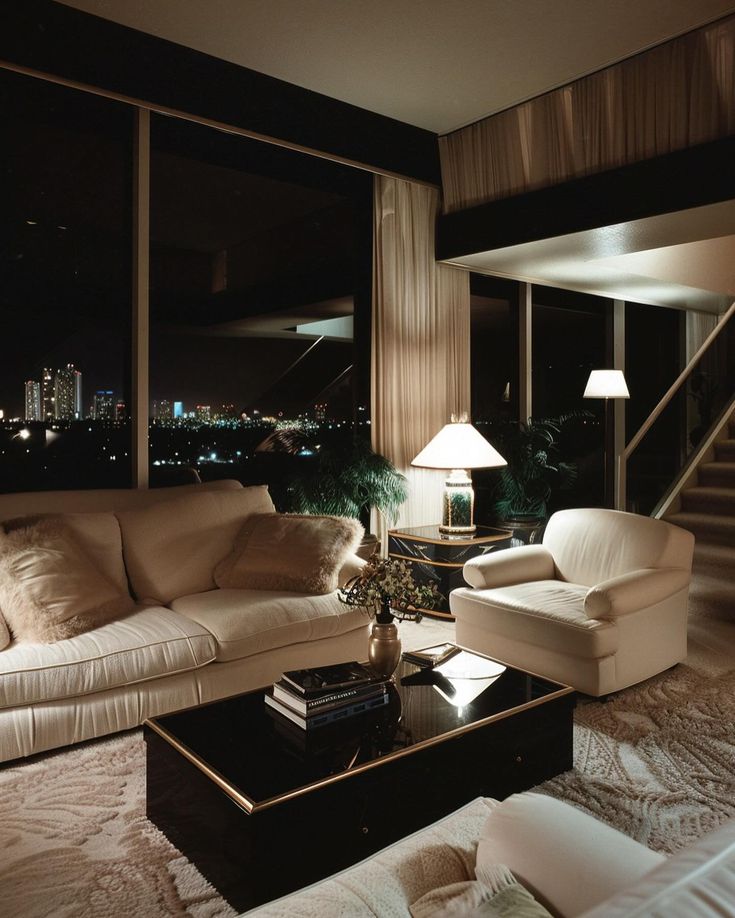 a living room filled with white furniture next to a window covered in night time lights