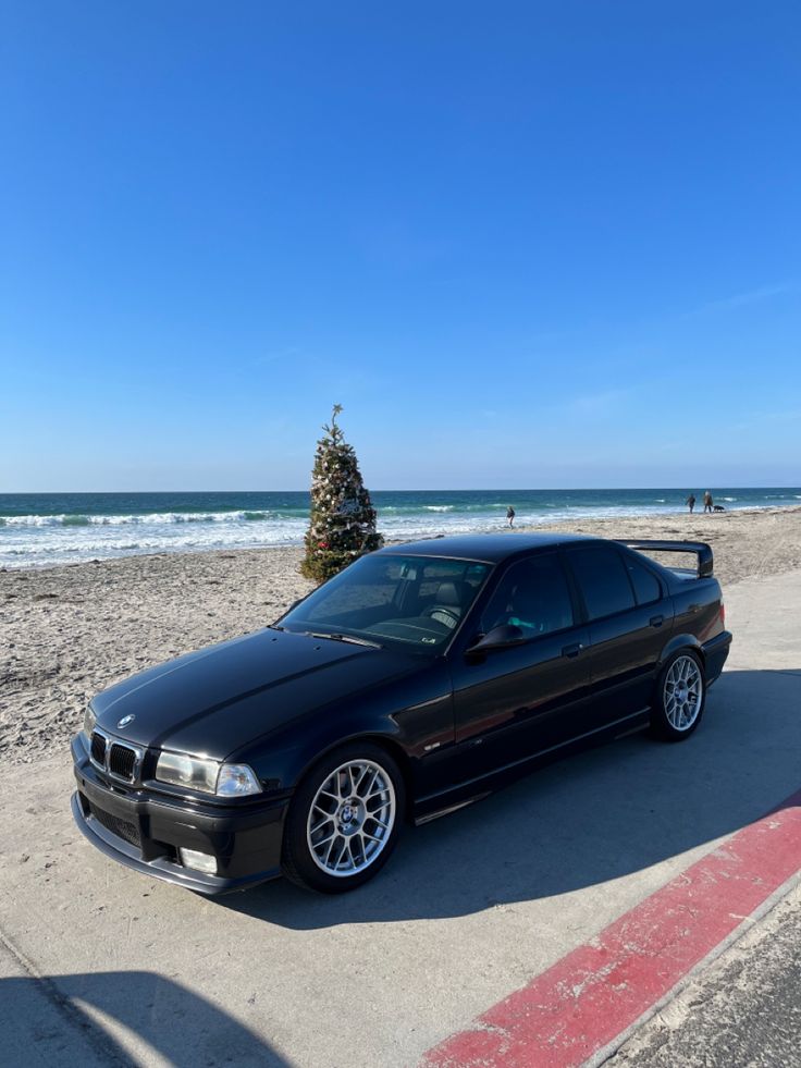 a black car parked on the beach next to a tree