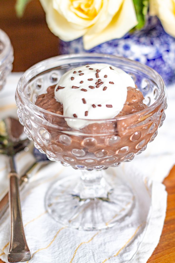 a dessert in a glass bowl on top of a table with flowers and spoons