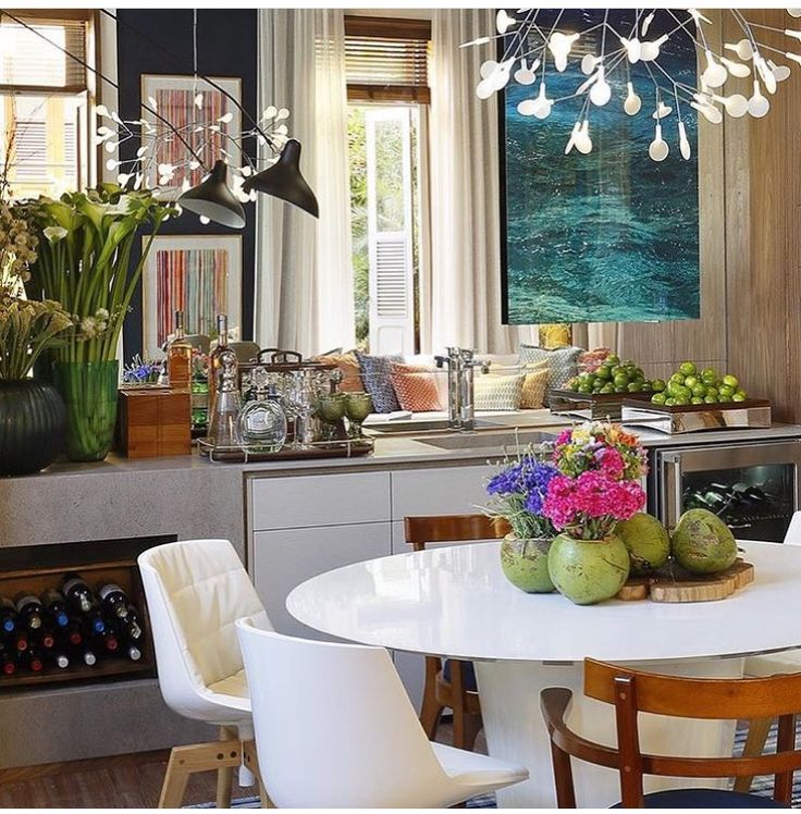 a dining room table with flowers and fruit on it in front of a kitchen island