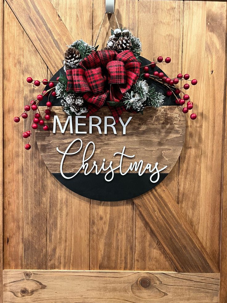 a merry christmas sign hanging on the side of a door with pine cones and red berries