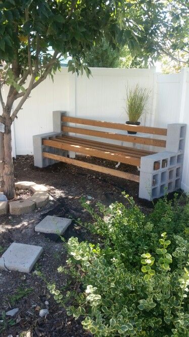 a wooden bench sitting under a tree next to a white fence and shrubbery on the side of a building