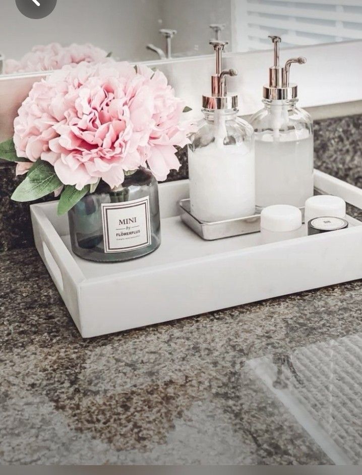 a bathroom sink with soap and lotion on the counter top next to a pink flower