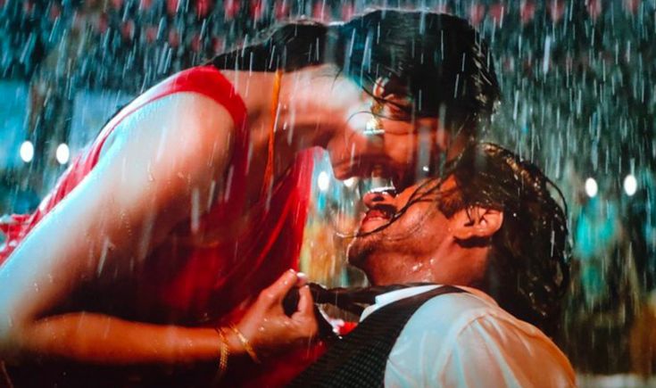 a man and woman standing in the rain under an umbrella with their faces close to each other