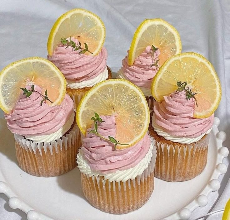 cupcakes with pink frosting and lemon slices on a white cake platter