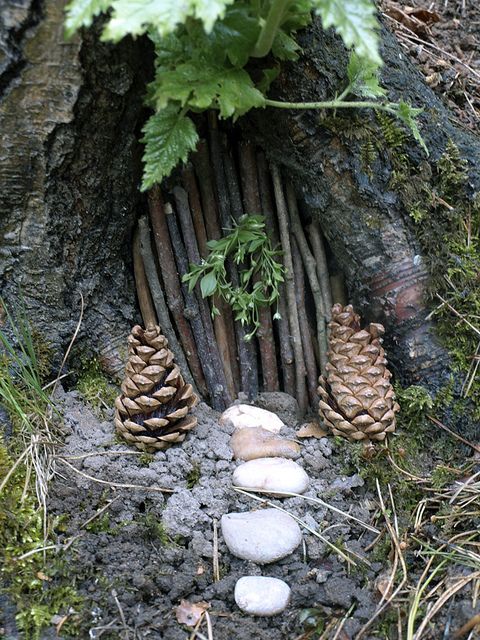 a fairy garden with pine cones, rocks and stones in the ground next to a tree trunk