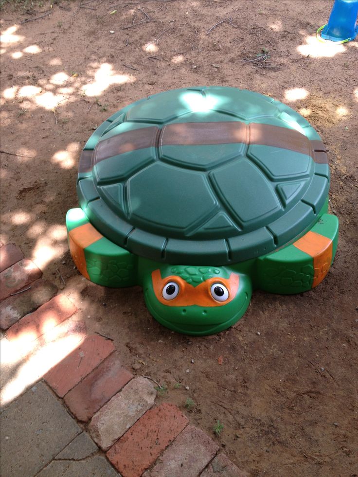 a turtle shaped toy sitting on top of a brick walkway next to a tree trunk