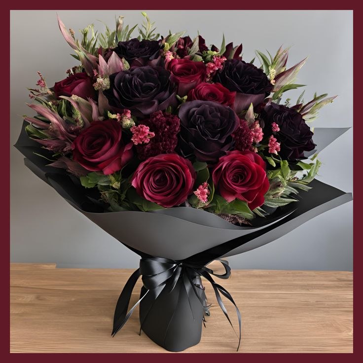 a bouquet of flowers is wrapped in black paper and tied with a bow on a wooden table