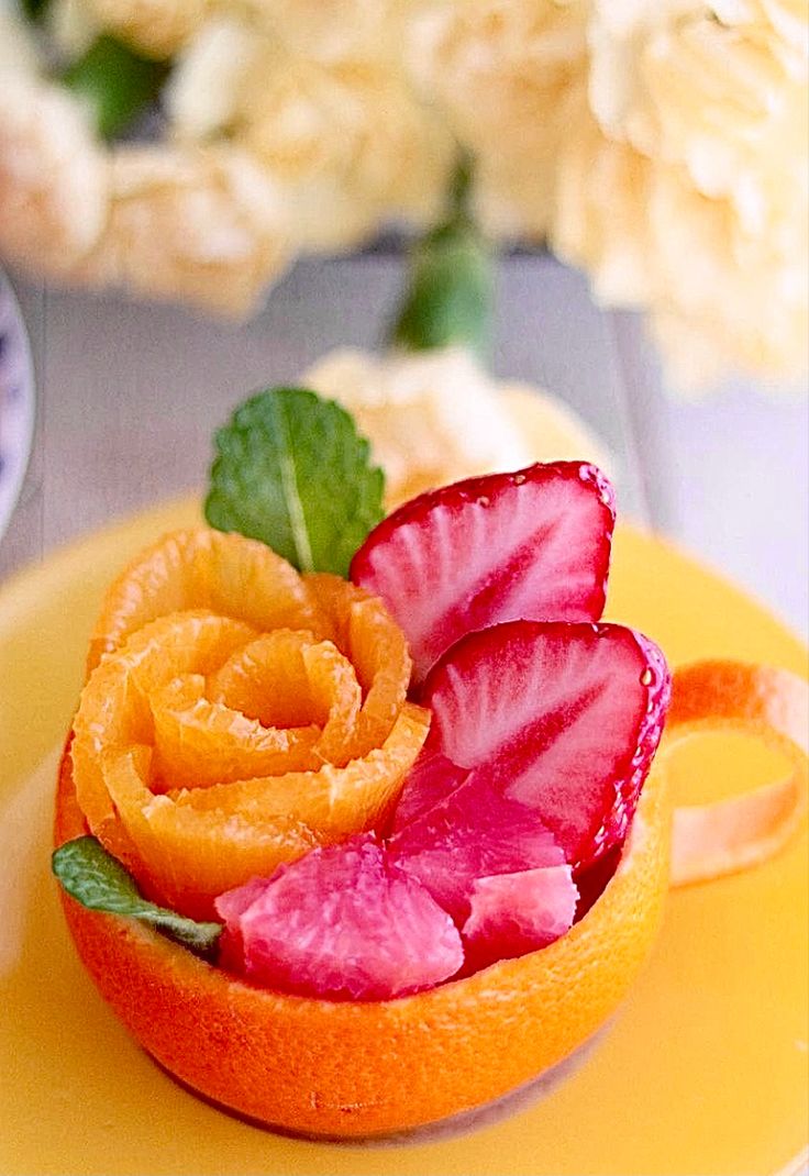 an orange with sliced fruit on it sitting on a yellow plate next to some flowers