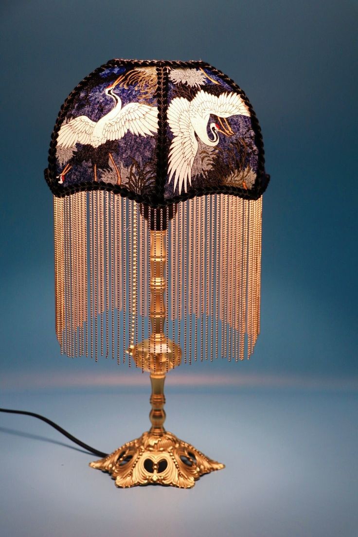 a table lamp with two white birds on it's sides and fringes hanging from the base