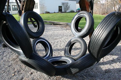 several tires stacked on top of each other in front of a building with grass and trees