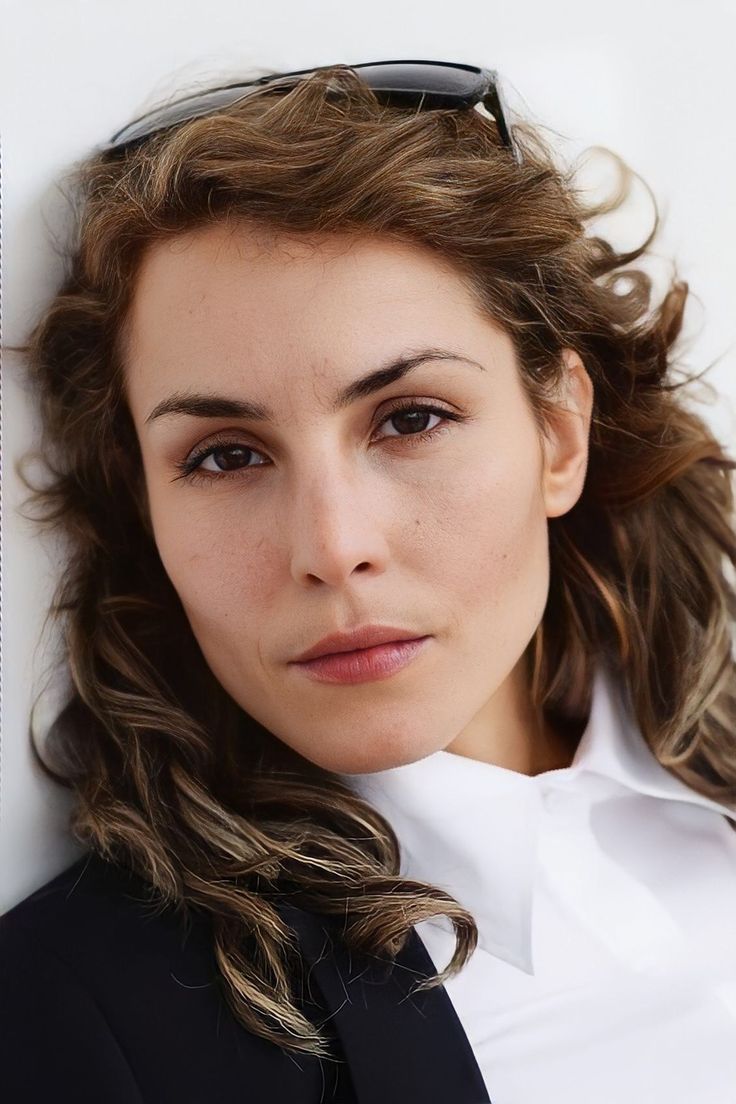 a woman in a suit and sunglasses leaning against a wall