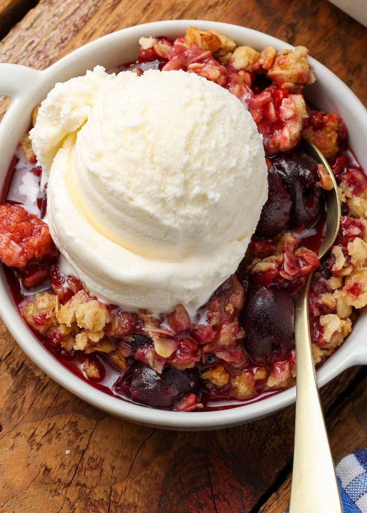 a bowl filled with fruit and ice cream on top of a wooden table next to a spoon