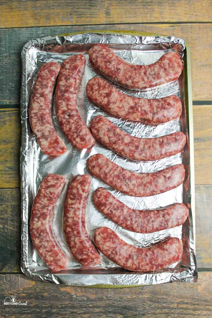 raw sausages on tin foil lined up on a wooden table