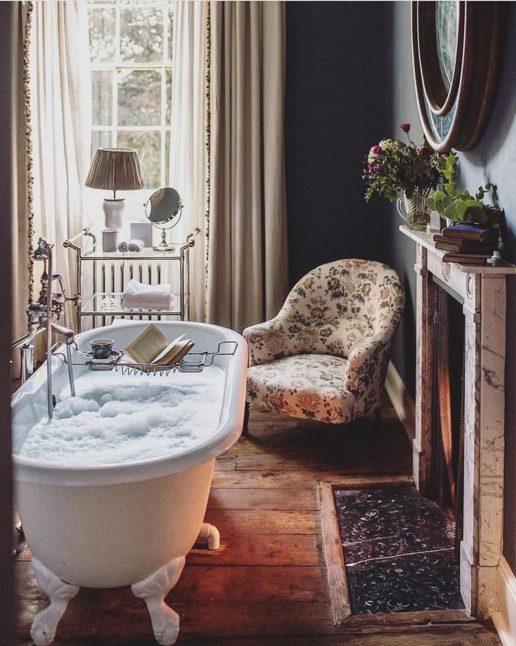 an old fashioned bathtub in the corner of a room with a chair and fireplace