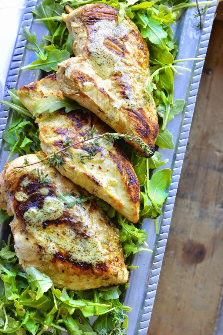 grilled chicken with herbs on a bed of lettuce in a metal tray