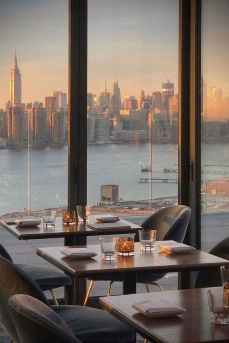 an empty restaurant with large windows overlooking the water and cityscape in the background