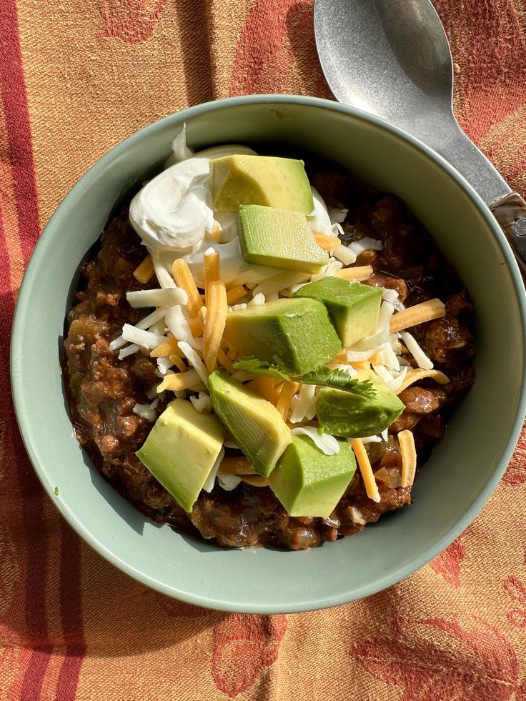 a bowl filled with chili, cheese and avocado on top of a table