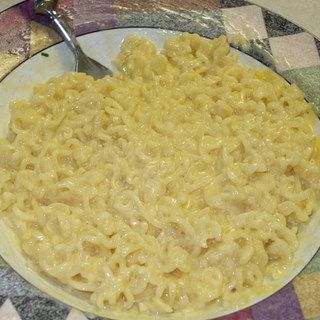 a plate full of macaroni and cheese on a checkered table cloth with a spoon