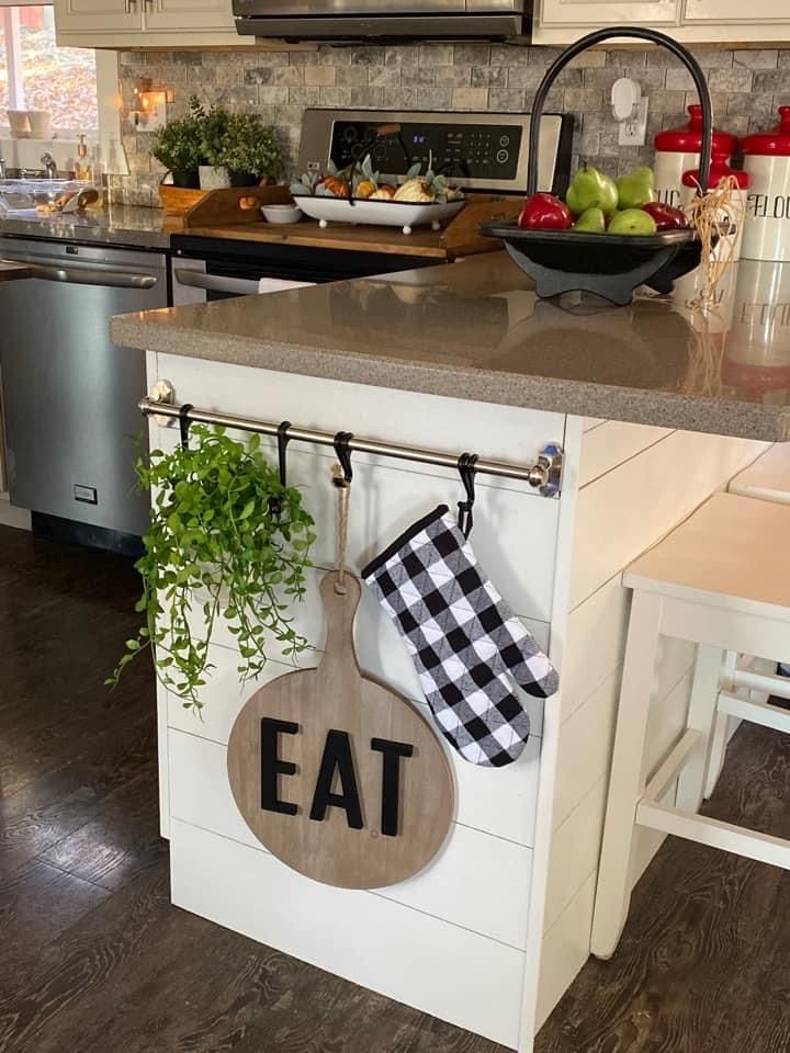 a kitchen island with an eat sign hanging from it's side and potted plants on the counter