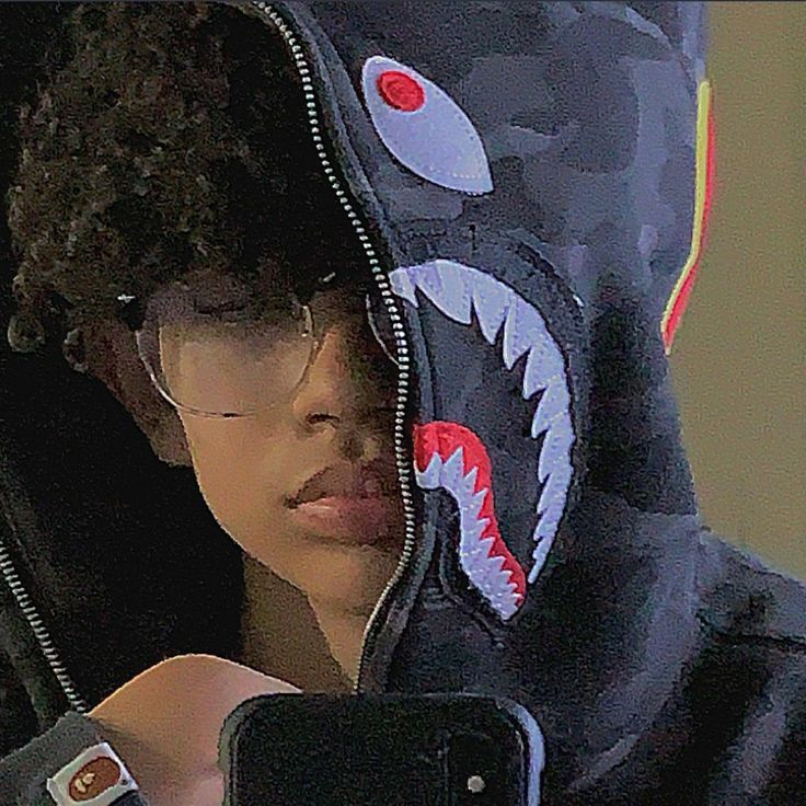 a young boy wearing a shark hoodie and holding a cell phone up to his ear