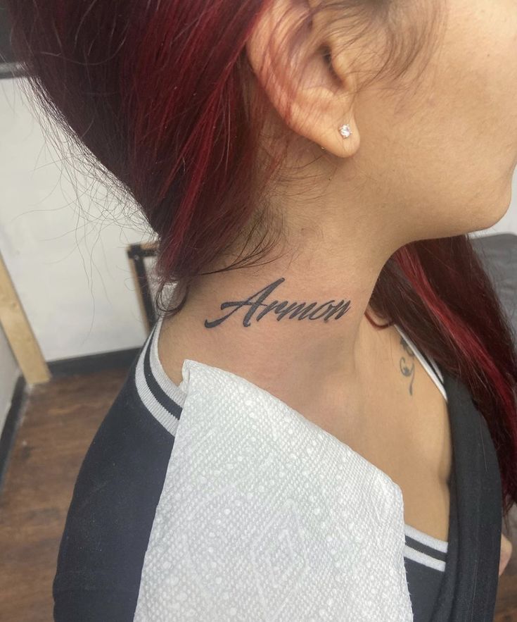 a woman with red hair has a name tattoo on her neck and behind her ear