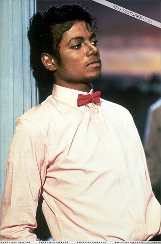 a young man wearing a red bow tie standing next to a pillar with his hands on his hips