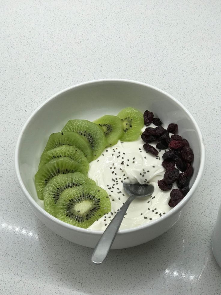 a bowl filled with yogurt, kiwi and raisins