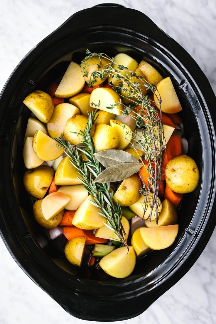 a crock pot filled with potatoes, carrots and rosemary garnishes