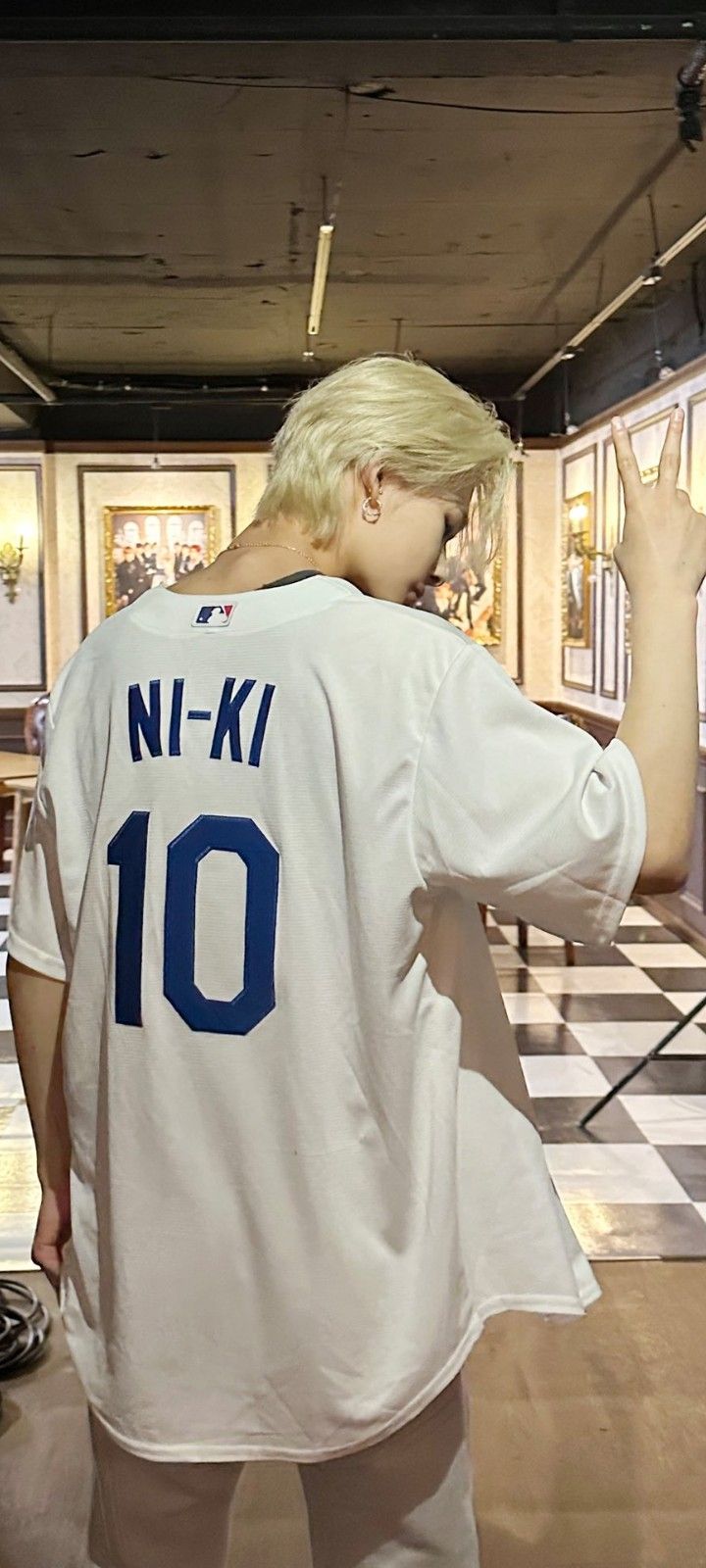 a man with blonde hair wearing a white baseball jersey standing next to a black and white checkered floor