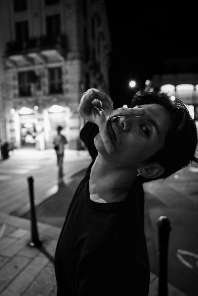 black and white photograph of a man on the street at night with his hand up to his face