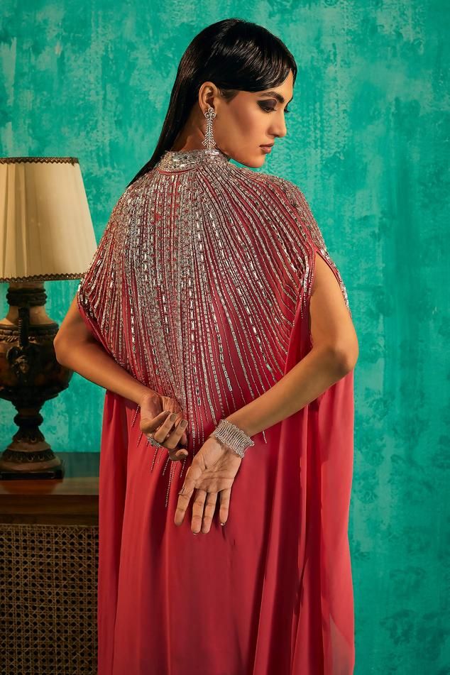 Hot pink georgette cape with intricate silver crystal embellishments and asymmetric sleeves. Paired with an embellished kurta and sharara.
Components: 3
Pattern: Embroidered
Type Of Work: Crystal, Bead
Neckline: High collared
Sleeve Type: Asymmetric
Fabric: Georgette
Color: Pink
Other Details: 
Model Height: 5 ft 7 inches, wearing size S
Occasion: Mehendi and Haldi, Sangeet - Aza Fashions Hand Embellished Blouse Piece For Party Wear, Party Wear Hand Embellished Blouse For Festive Season, Festive Hand Embellished Party Wear Blouse Piece, Festive Hand Embellished Party Wear Blouse, Semi-stitched Hand Embellished Georgette Blouse Piece, Hand Embellished Semi-stitched Georgette Blouse Piece, Hand Embellished Sharara For Evening Party Wear, Party Dupatta With Zari Work And Cape Sleeves, Floor-length Evening Sets With Dabka Work