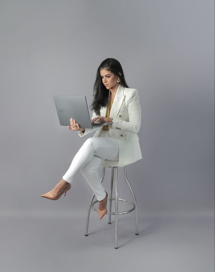 a woman sitting on a stool using a laptop computer