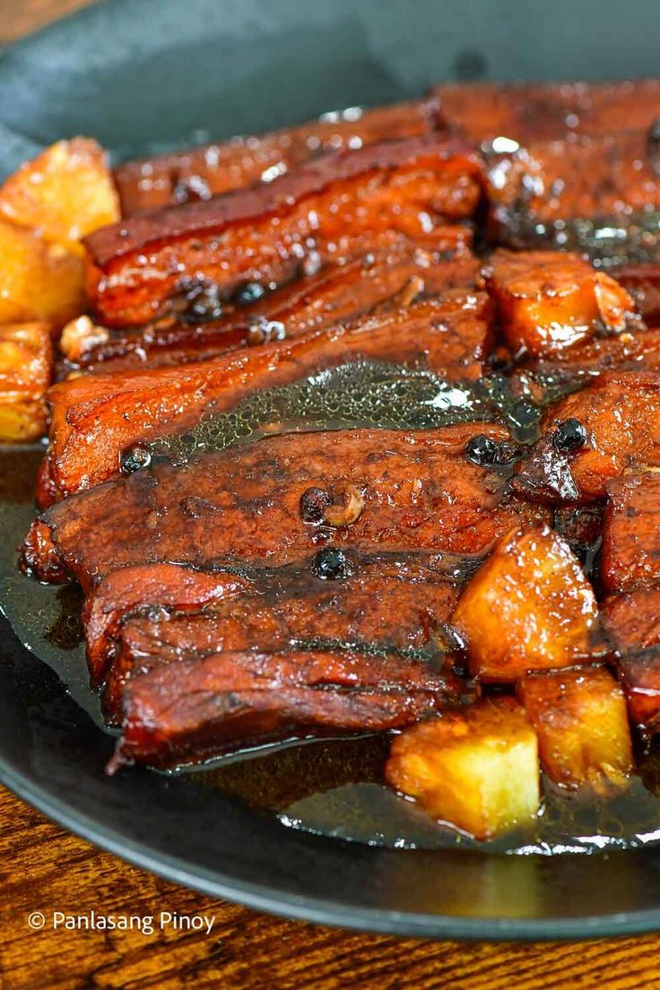 some meat and potatoes are cooking in a skillet on a wooden table with chopsticks