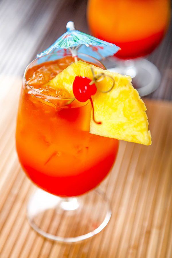 two glasses filled with drinks on top of a wooden table next to an umbrella and pineapple