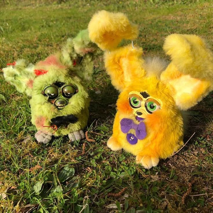 two stuffed animals sitting in the grass with one looking like it's being chased by another