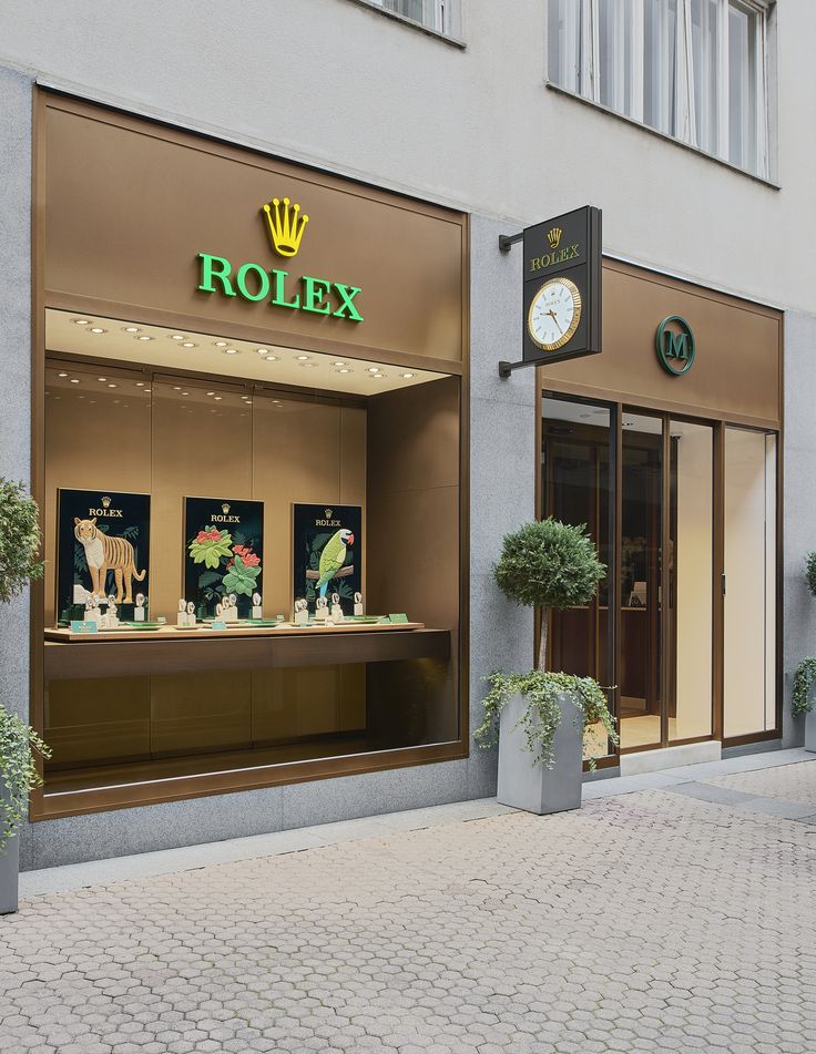 a rolex store front on a cobblestone street with potted plants in the window