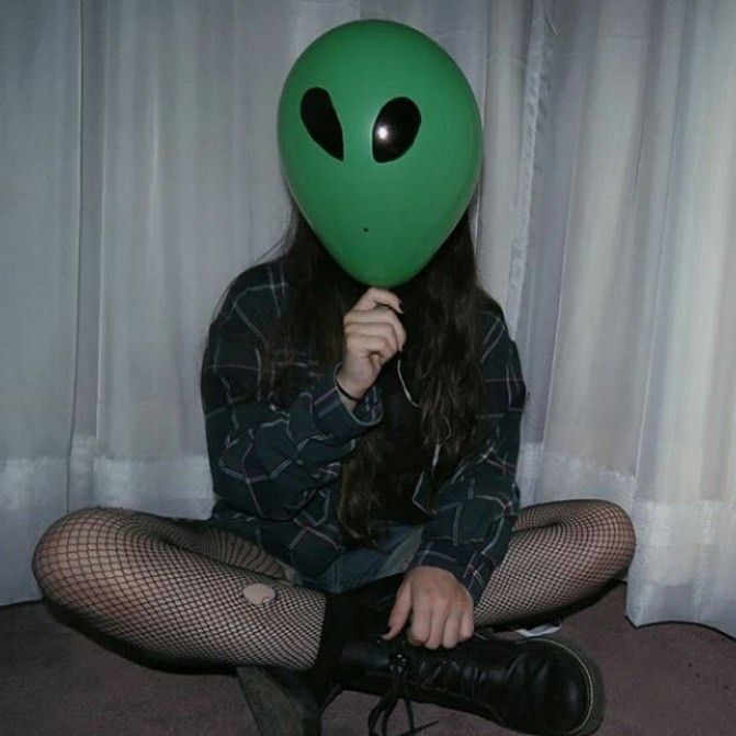 a woman sitting on the floor wearing a green alien mask