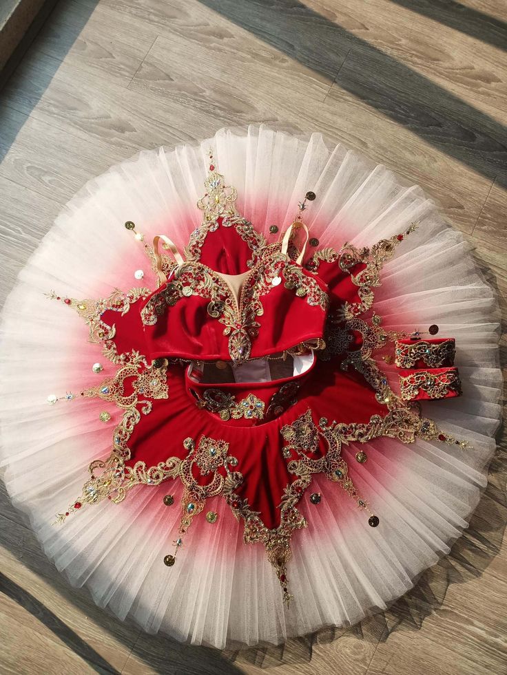 a red and white tutu with gold trimmings sits on a wooden floor