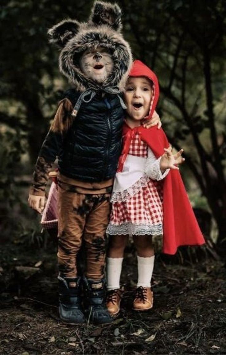 two children dressed up in costumes standing next to each other on the forest floor with trees behind them