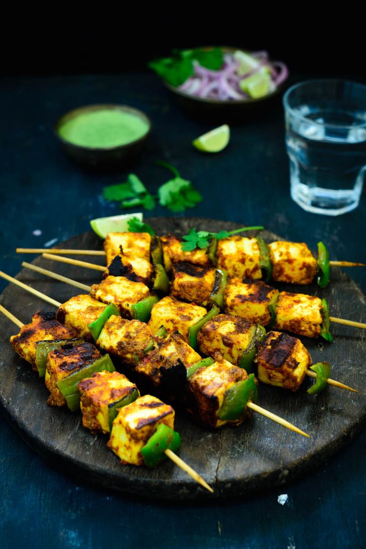 several skewers of food sitting on a wooden plate next to a glass of water