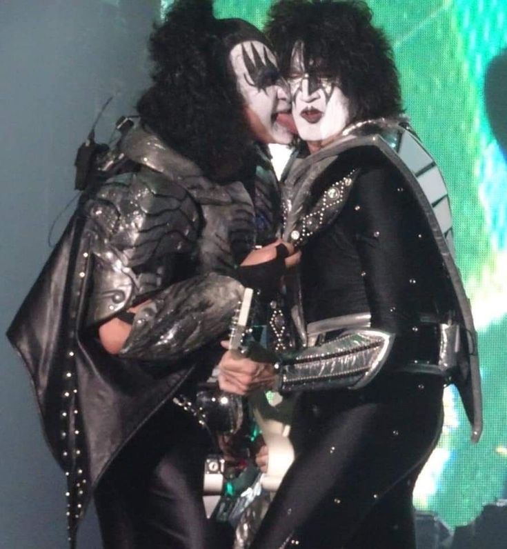 kiss band members kissing on stage at a concert in black and white makeup, one with his mouth open