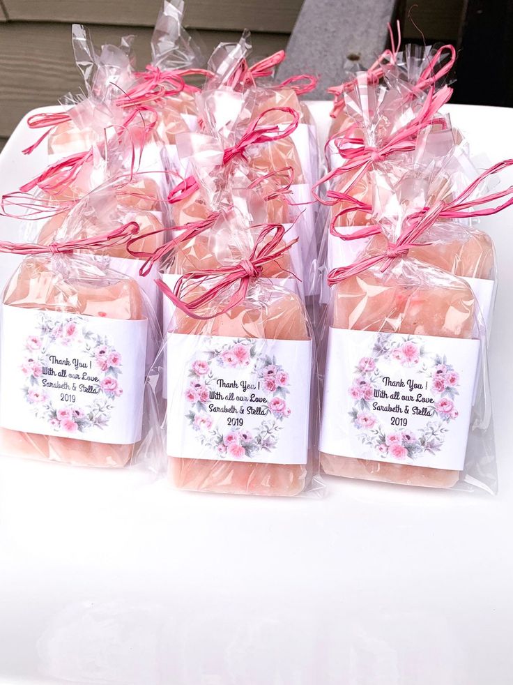 four soaps wrapped in plastic bags with pink ribbons on them sitting on a table