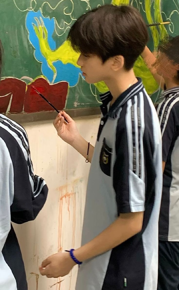 two young boys standing in front of a chalkboard with writing on it and one boy holding a paintbrush