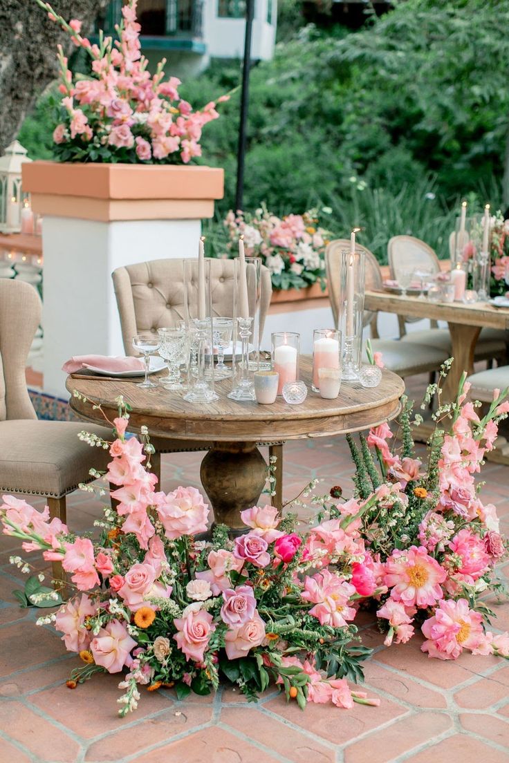 a table with flowers and candles on it in front of some chairs at an outdoor event