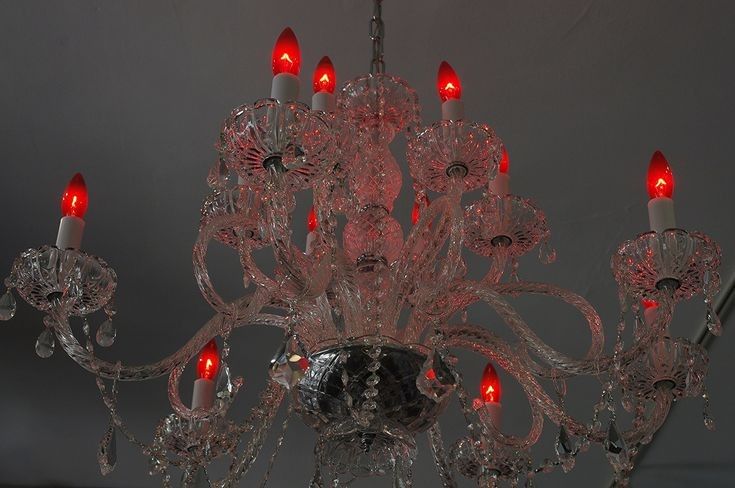 a chandelier with red candles hanging from it's sides and the lights turned on